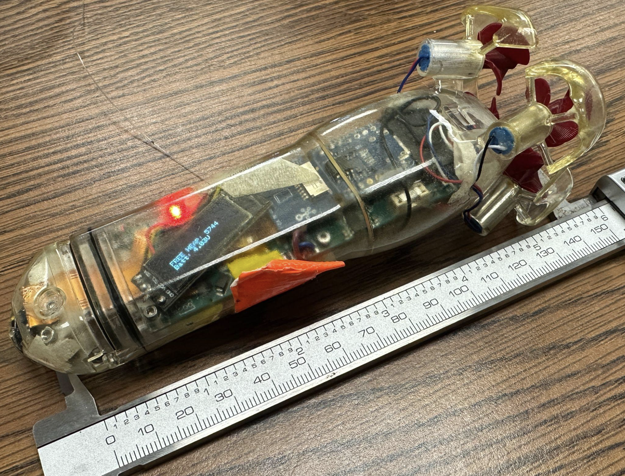 The assembled autonomous torpedo, a transparent cylindrical vehicle with four propellers, next to calipers